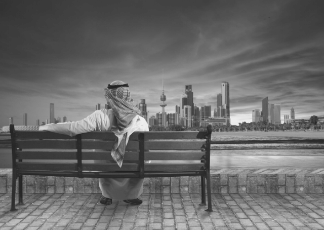Man zittend op een bankje kijkend naar Koeweit-stad
